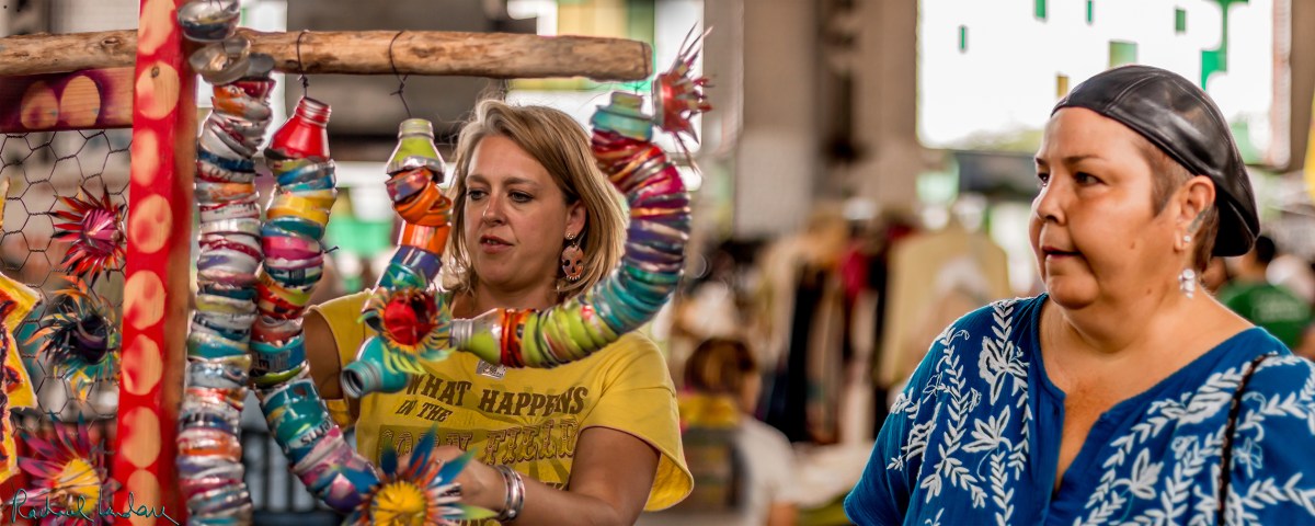 Double-wide image of Autumn the artist helping a customer select a folk art piece