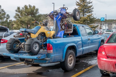 A pickup truck with two ATVs in its flatbed is in a parking space